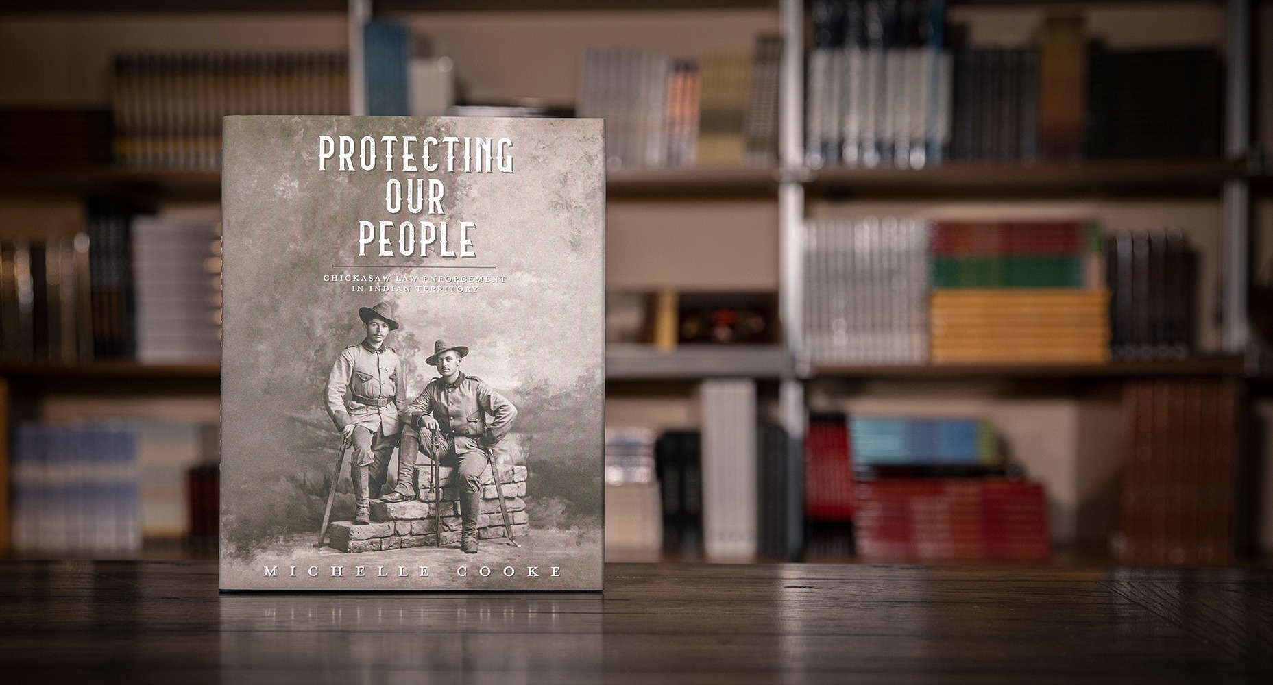 The book "Protecting our People" on display in front of bookshelves.