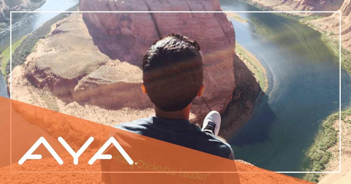 A boy sits atop a cliff edge, overlooking scenic rocks below and a peaceful flowing river.