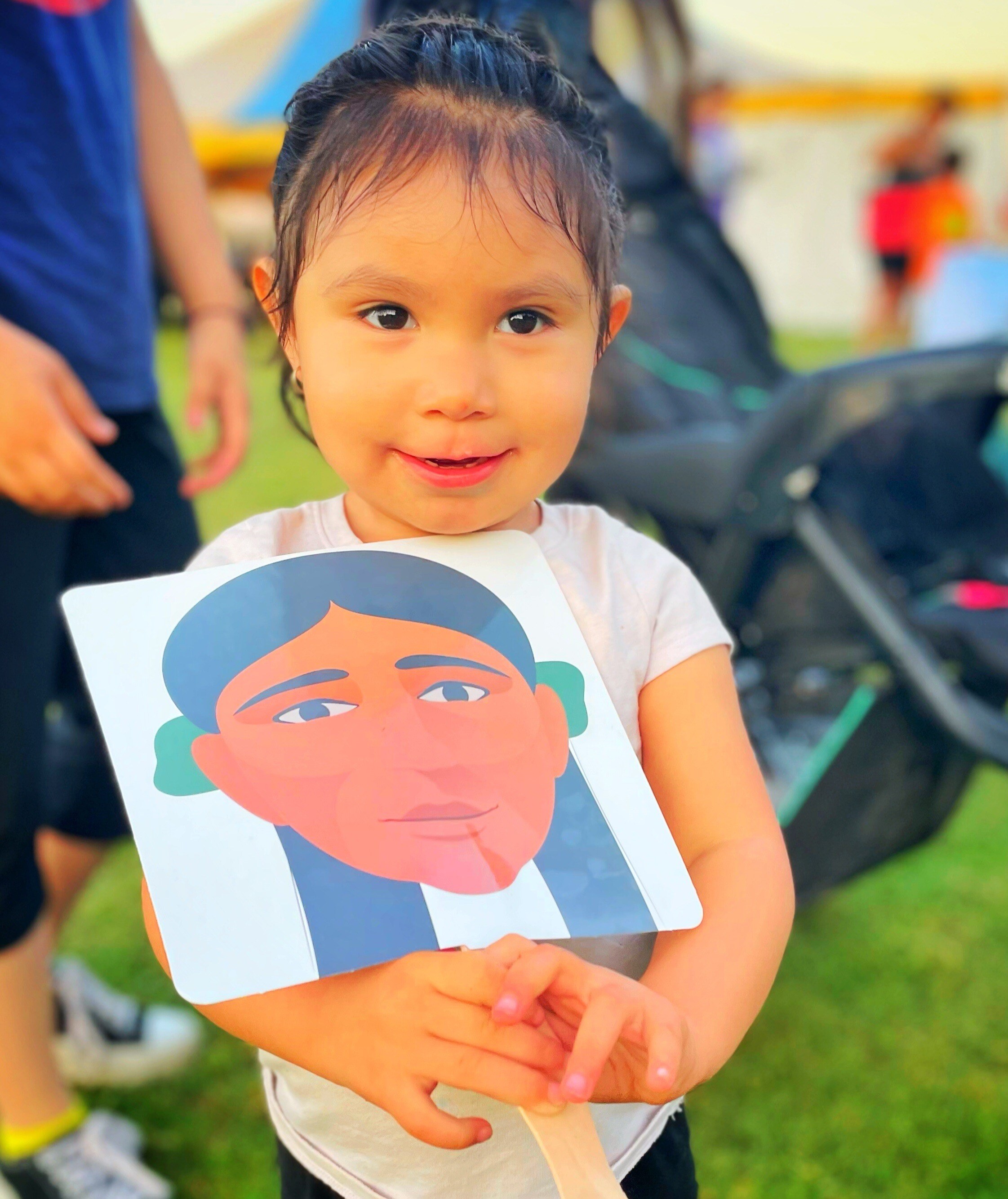 A young girl holding a fan with Eliza's, an AYA Walking Partner, face on it. 