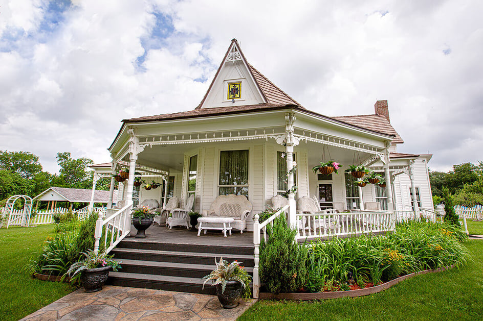 Governor Johnston’s home, the Chickasaw White House. Pictured is the white house with a wrap around porch with wicker furniture and hanging plants. 