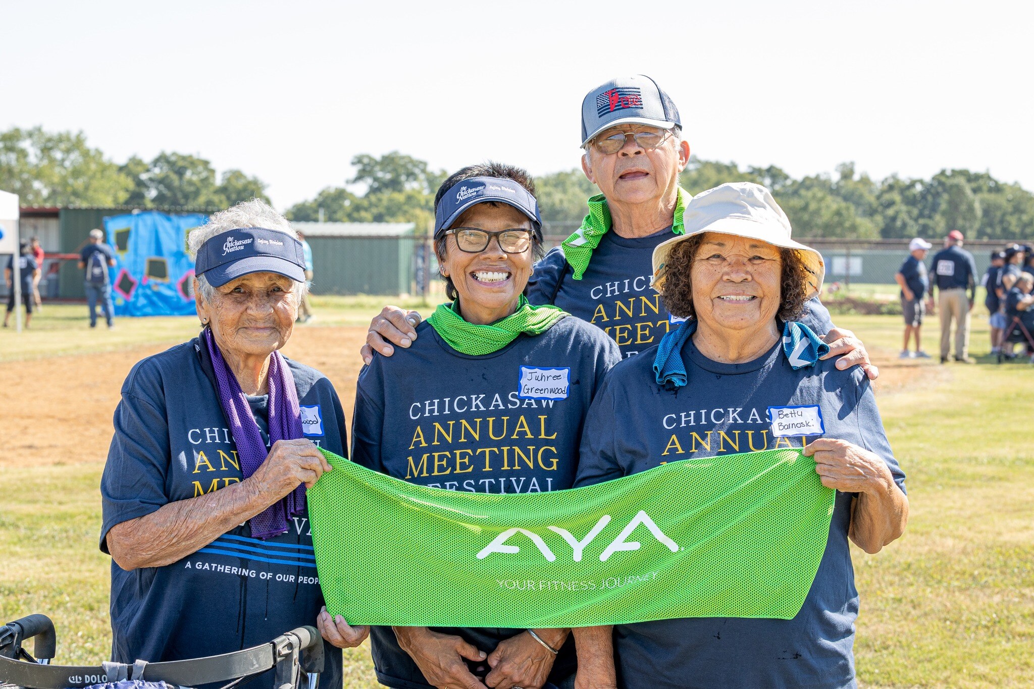 A group of Chickasaw citizens in Annual Meeting & Festival t-shirts holding a green AYA cooling towel.