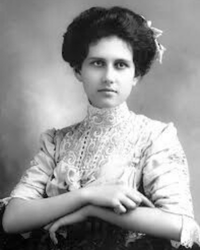 A black and white portrait of young Muriel Hazel Wright wearing a high-necked Victorian-style lace blouse, her dark curly hair styled up, gazing directly at the camera with a poised, confident expression.